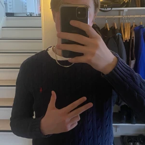 Blå kabelstickad tröja från Ralph Lauren - PRIS KAN DISKUTERAS                                            Säljer en stilren blå kabelstickad tröja från Ralph Lauren med det klassiska röda logotypen på bröstet. Tröjan har långa ärmar och ribbade muddar vid ärmslut och nederkant. Perfekt för en avslappnad men snygg look.