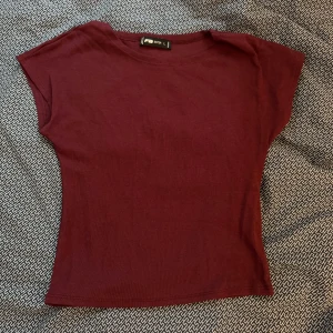 Vinröd topp från Zara - Säljer en stilren vinröd topp. Den har en enkel design med korta ärmar och en rund halsringning. Perfekt för en avslappnad look eller att klä upp med accessoarer. Passar bra till både jeans och kjol. Storlek L men skulle säga att den passar till en S. Aldrig använd. 