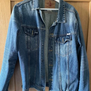 Blå jeansjacka från Emmett - Klassisk blå jeansjacka från Emmett med knappar framtill och två bröstfickor. Perfekt för en avslappnad stil. Jackan har en tidlös design och passar till många olika outfits.