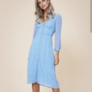 Blå Paris-klänning med knappar - Säljer en elegant blå Paris-klänning med ett subtilt mönster och knappar framtill. Klänningen har långa ärmar och en v-ringad design som ger en stilren look. Perfekt för en chic och modern stil. Nypris 1495kr, använd 1 gång.🌸 strlk 40 men passar mer som en 38!! Pris kan diskuteras :)