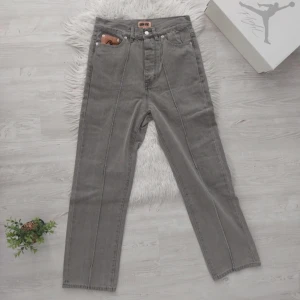 Gråa Corteiz Jeans - Snygga grå jeansbyxor från Corteiz med unika broderade stjärnor och måne på baksidan. Byxorna har en rak passform och klassisk femficksdesign. Perfekta för dig som vill ha något annorlunda i garderoben!