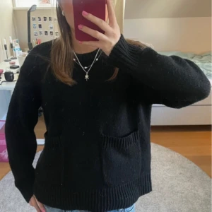 Svart stickad tröja med fickor - Säljer en svart stickad tröja med långa ärmar och praktiska fickor framtill. Perfekt för kyligare dagar och enkel att matcha med olika outfits. Tröjan har en klassisk design med ribbstickade muddar vid ärmslut och nederkant.