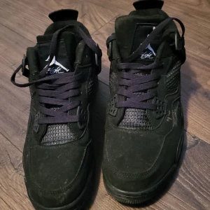 Svarta Nike Air Jordans - Säljer ett par svarta Nike Air Jordans med snörning och rund tå. Skorna har en stilren design med mockadetaljer och ikonisk logga på plösen. Perfekta för dig som vill ha en klassisk sneaker med en modern touch.