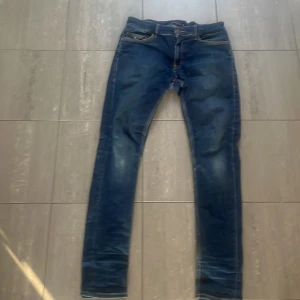 Blå jeans från Tommy Hilfiger - Snygga blå jeans från Tommy Hilfiger med klassisk femficksdesign och subtila slitningar. De har en normal passform och är perfekta för en avslappnad stil. Märkesdetaljer syns på bakfickan och insidan av linningen. Nypris 1700 modell: 179cm och 65kg