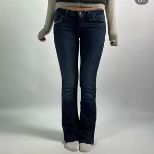 Mörkblå bootcut jeans med nitar - Snygga mörkblå bootcut jeans med coola nitar vid fickorna. Perfekta för en trendig look. De har en klassisk femficksdesign och knappgylf. Defekter på de 2 sista bilderna  