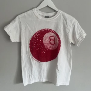 Vit t-shirt med rött tryck - Säljer en vit t-shirt med ett coolt rött tryck av en boll med siffran 8 och texten 'In Print We Trust'. Perfekt för en avslappnad stil.