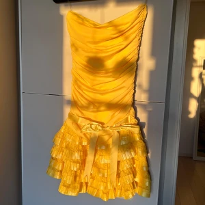 Vintage klänning - Säljer en fantastisk gul klänning från LISA med draperad överdel och volangdetaljer på kjolen. Klänningen har en vacker rosett i midjan och är perfekt för sommarens fester. Den korta längden och den ljusa färgen gör den till ett blickfång.