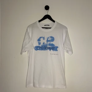 C.P. Company T-shirt - Säljer en stilren vit t-shirt från C.P. Company med ett blått tryck på framsidan. T-shirten är kortärmad och har en normal passform. Perfekt för en avslappnad look. Den är i nyskick och tags finns med. 