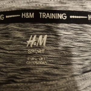 Grå träningshoodie från H&M - Säljer en gråmelerad träningshoodie från H&M. Perfekt för träning med sin bekväma passform och mjuka material. Hoodien har långa ärmar och en klassisk design som passar till alla träningspass.