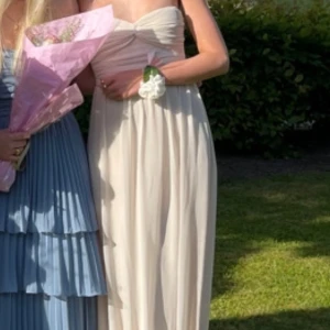 Vit/begiefärgad axelbandslös klänning - Vit/begie axelbandslös klänning med draperad detalj vid bysten. Perfekt för en somrig bal eller fest. Klänningen har en flytande lång design som ger en vacker siluett. Pris kan diskuteras 