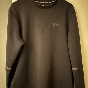 Svart tröja från Under Armour - Säljer en stilren svart tröja från Under Armour. Tröjan har långa ärmar och en diskret logga på bröstet. Perfekt för träning eller vardagsbruk. Nypris: 1.200