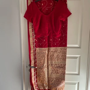 Röd traditionell klänning med gulddetaljer - Elegant röd sari med gulddetaljer och mönster. Från Sti Lanka. Aldrig använd