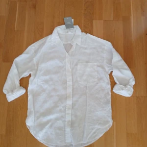 Vit linneskjorta från H&M, strl XS - Säljer en stilren vit linneskjorta från H&M. Skjortan har en klassisk krage och knappar framtill. Perfekt för en avslappnad och elegant look. Den är långärmad och tillverkad i ett lätt och luftigt linne.