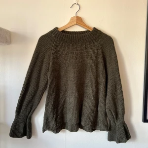 Olivgrön stickad tröja från Gina Tricot - Säljer en mysig olivgrön stickad tröja från Gina Tricot. Tröjan har en ribbad struktur med utsvängda ärmar nedtill. 
