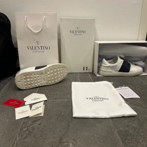 Valentino Garavani sneakers - PRIS KAN DISKUTERAS! (Tar även emot byten)Snygga Valentino Garavani sneakers i vitt med en bred mörkblå rem över ovansidan. Skorna har snörning och en rund tå, vilket ger en stilren look. Perfekta för dig som vill ha en exklusiv touch på vardagsstilen. Jag har valt att sälja dessa eftersom jag får ingen användning av dem längre då jag har andra skor att välja på. 