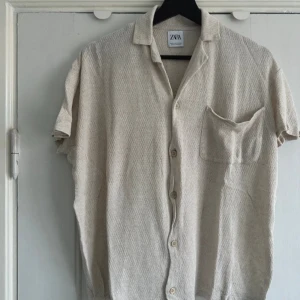 Beige kortärmad skjorta från Zara - skjorta från Zara med korta ärmar och knappar framtill. 