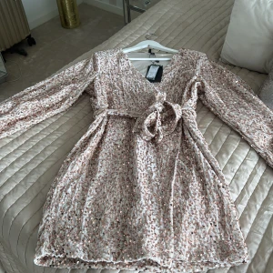Champagnefärgad paljettklänning från Vero Moda - Säljer en glittrig champagnefärgad klänning från Vero Moda. Klänningen har långa ärmar och ett knytband i midjan för en omlott-look. Perfekt för att glänsa på festen! ✨Köpte fel storlek. 