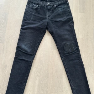 Acne studios Svarta jeans med korsdetaljer  - Snygga svarta jeans med unika korsdetaljer på knä och bakficka. De har en slim passform och är tillverkade i ett bekvämt denimtyg. Perfekta för att ge din outfit en edgy touch. Med chrome hearts patched work