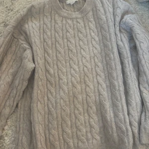 Grå kabelstickad tröja från H&M - Säljer en mysig grå kabelstickad tröja från H&M. Tröjan har en klassisk rund hals och långa ärmar, perfekt för kyliga dagar. Den är både stilren och bekväm, ett måste i garderoben! 🧶
