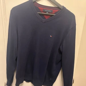 Mörkblå tröja från Tommy Hilfiger - Snygg mörkblå tröja från Tommy Hilfiger med v-ringning och diskret logga på bröstet. Perfekt för en stilren look. Tröjan har långa ärmar och är tillverkad i ett mjukt material.