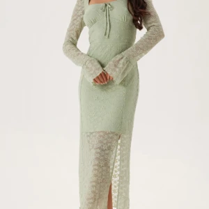 Ljusgrön spetsklänning med slits - Säljer en elegant ljusgrön långklänning med spetsdetaljer och långärmade ärmar. Klänningen har en snygg slits framtill och en söt knytning vid bysten. Perfekt för dig som gillar romantisk stil och vill sticka ut med en unik färg. Den är aldrig använd. Prislapp på 