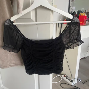 Svart mesh croppad topp med puffärm - Säljer en svart croppad topp i xs, man kan ha den som både of shoulder och upp på axlarna. 