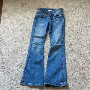 Blå bootcut jeans från Gina Tricot Young  - Snygga blå bootcut jeans från Gina Tricot med klassisk femficksdesign och broderad bakficka. Jeansen har låg midja och är tillverkade i jeansmaterial med lätt slitning för en cool look.