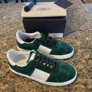 Valentino Garavani gröna sneakers - Snygga sneakers från Valentino Garavani i mörkgrön mocka med vita detaljer och vita sulor. Klassisk låg modell med rund tå och gröna snören. Perfekta för dig som vill sticka ut med stilrena och exklusiva skor.