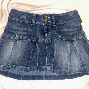 Mörkblå jeanskjol med veck - Säljer en snygg mörkblå jeanskjol med markerade veck och dubbla knappar framtill. Midjebredden är 37 cm men den är väldigt strechig så passar mig som har 40 cm. S/M. Kan mötas upp i Stockholm🩷