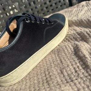 Svarta sneakers från Lanvin i mocka och skinn - Snygga marinblåa sneakers från Lanvin med ovandel i mocka och tåparti i skinn. Klassisk låg modell med rund tå, vita sulor och marinblåa snören. Perfekta för dig som gillar stilrena och exklusiva sneakers med premiumkänsla. Pris går att diskuteras vid snabb affär!🙌