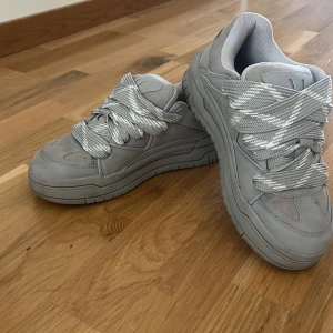 Bershka grå skor - Stilrena grå sneakers med breda, mönstrade snören och chunky sula. Ovandelen är i en mix av syntet och mesh för extra komfort och andningsförmåga. Perfekta för dig som gillar en modern och sportig look.