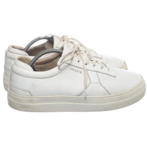 Vita sneakers från Axel Arigato - Stilrena vita sneakers från Axel Arigato med klassisk låg profil och snörning. Skorna är tillverkade i skinn och har en platt sula samt diskret logga på sidan. Perfekta för en clean och modern look.