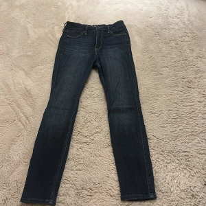 Mörkblå skinny jeans Hollister W27 L26 - Snygga mörkblå skinny jeans från Hollister med hög midja och klassiska gula sömmar. Jeansen har fem fickor och diskret Hollister-logga på bakfickan. Perfekta för dig som gillar en tight passform och stilren look.