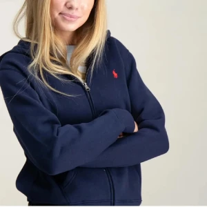 Mörkblå hoodie från Polo Ralph Lauren - Snygg mörkblå hoodie från Polo Ralph Lauren med röd broderad logga på bröstet. Tröjan har huva, dragkedja framtill och två fickor. Perfekt för chill dagar och enkel att matcha med jeans eller kjol. Tröjan är köpt för 1200kr, pris är självklart diskuterbart💓 Storleken är L för barn, men skulle säga att den passar Xs-M