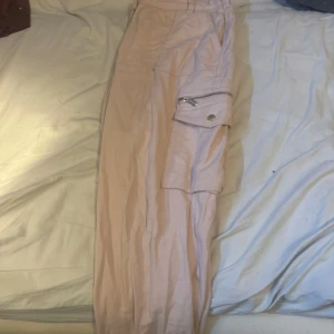 Beiga cargopants med dragkedja - Säljer ett par beiga cargopants med stora fickor på sidorna och snygga dragkedjedetaljer. Byxorna har avslappnad passform och är perfekta för en chill streetwear-look. Tillverkade i ett lätt bomullsmaterial som är skönt att bära hela dagen.