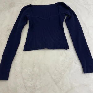 Mörkblå stickad långärmad topp - Snygg mörkblå stickad topp med lång ärm och markerad byst. Toppen har en figurnära passform och fyrkantig halsringning som ger en modern vibe. Perfekt att styla med jeans eller kjol för en trendig look.