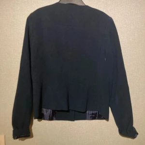 Mörkblå kavaj med rund hals - Stilren mörkblå kavaj med rund halsringning och mörkblå utsida. Jackan har långa ärmar och ett diskret innerfoder med ränder. Perfekt för dig som gillar en clean look och vill ha något som funkar till många outfits.