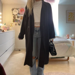 Svart kappa från Monki XS - Lång svart kappa från Monki i storlek XS. Klassisk rak modell med knappar framtill och krage. Perfekt oversized vibe och passar till allt. Snygg att slänga över jeans och crop top för en chill men stilren look.