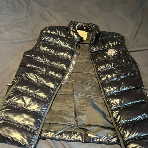 Monclerliknade dunväst  - Säljer min killes Monclairliknande väst då han inte längre använder den. Den är i S men passar M. Bra skick men lite tråd har släppt på ena sidan vid dragkedjan, se bild 2💕 Han kan gå ner lite i pris beroende på snabb och smidig affär🤩Skriv vid frågor🥹