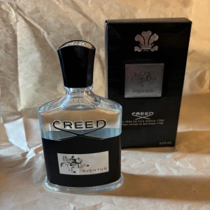  Aventus Eau de Parfum 100ml -  Aventus parfym 100ml. Flaskan är genomskinlig med svart etikett och silverdetaljer, och har en svart kork. Kommer i svart kartong med silverlogga.