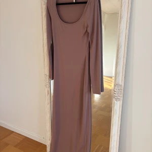 Beige långklänning från Nelly XS - Säljer en stilren beige långklänning från Nelly i storlek XS. Klänningen har lång ärm och en djup rundad halsringning. Några små prickar på den som jag inte vet vad de är