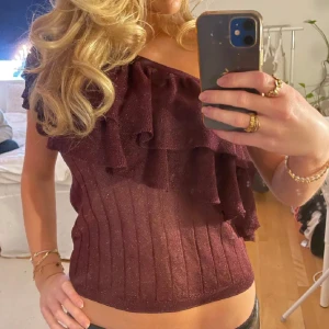 Glittrig vinröd oneshoulder topp - Supersnygg vinröd topp med glittrigt tyg och volangdetaljer. Modellen är oneshoulder vilket ger en trendig look. Från Mango i strl S💕