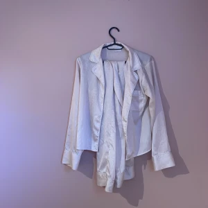 Ljusbeige/rosa pyjamas med leopardmönster - Säljer en lyxig ljusbeige/rosa pyjamas med diskret leopardmönster. Pyjamasen har klassisk krage, bröstficka och långa ärmar med breda manschetter. Materialet är glansigt och mjukt, perfekt för en chill och trendig look.