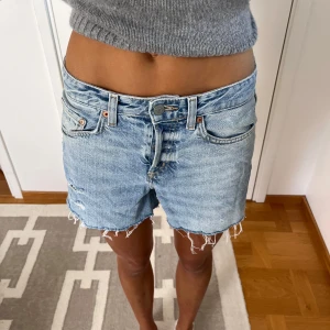 Ljusblå jeansshorts  - Snygga ljusblå jeansshorts med råa, fransiga kanter och klassisk femficksdesign. Modellen är högmidjad och har slitna detaljer framtill för en cool vibe. Perfekta för varma dagar och enkel att matcha med din favorittröja.