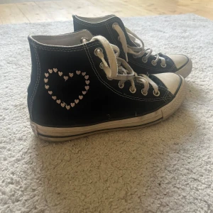 Converse All Star svarta med hjärtan - PRIS ÄR DISKUTERBART VID SNABBT KÖP!💗Svarta Converse All Star high tops med vita snören och sula. Skorna har broderade hjärtan i rött och vitt runt loggan och på sidan, samt texten 'me' broderad vid hälen. Klassisk rund tå och platt sula i gummi. Perfekt för dig som gillar unika detaljer och streetstyle.