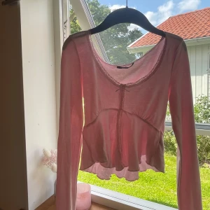Ljusrosa blus med spets från Gina Tricot - Supersöt ljusrosa blus från Gina Tricot i storlek xs.Använd kanske 3 gånger. Tröjan har lång ärm, v-ringad hals med spetskant och liten rosett framtill. Tröjan är croppad med volang nertill.Den är slut överallt och original pris var 260kr