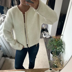 Vit stickad kofta i mjuk ull - Säljer en vit, fluffig och stickad kofta med rund hals och raka ärmar. Koftan är gjord i mjuk ull och har en enkel, clean look utan knappar eller dragkedja. Perfekt att slänga på över en t-shirt för en chill och stilren vibe. Har blivit lite knottrig men inget som märks mycket 
