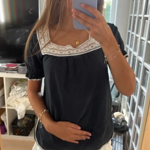 Mörkblå blus med spetsdetaljer - Supersöt mörkblå blus med korta puffärmar och bred vit spets runt den fyrkantiga ringningen. Blusen har även små spetsdetaljer vid ärmsluten och en luftig passform!!💕