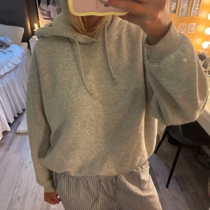 Grå hoodie från H&M i storlek M - En basic ljusgrå hoodie från H&M i storlek M. Tröjan har huva med snörning, ribbade muddar och en loose fit.