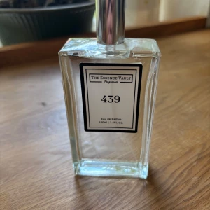The Essence Vault 439 Eau de Parfum - Säljer en stilren parfymflaska från The Essence Vault, nummer 439. Flaskan är genomskinlig och fyrkantig med en silverfärgad spraykork. Innehåller 100 ml Eau de Parfum. Perfekt för dig som gillar eleganta och minimalistiska doftflaskor.